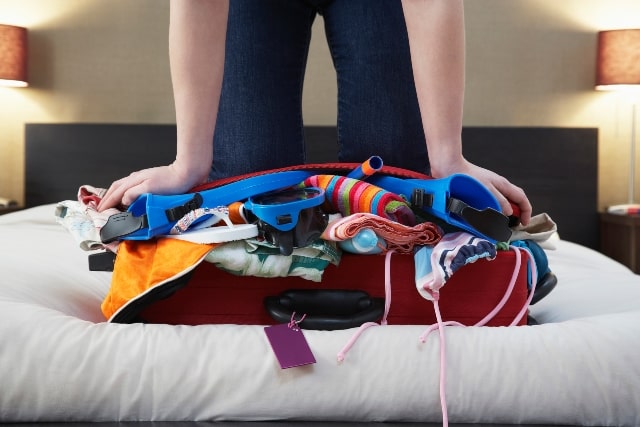 woman struggling to close an over filled suitcase